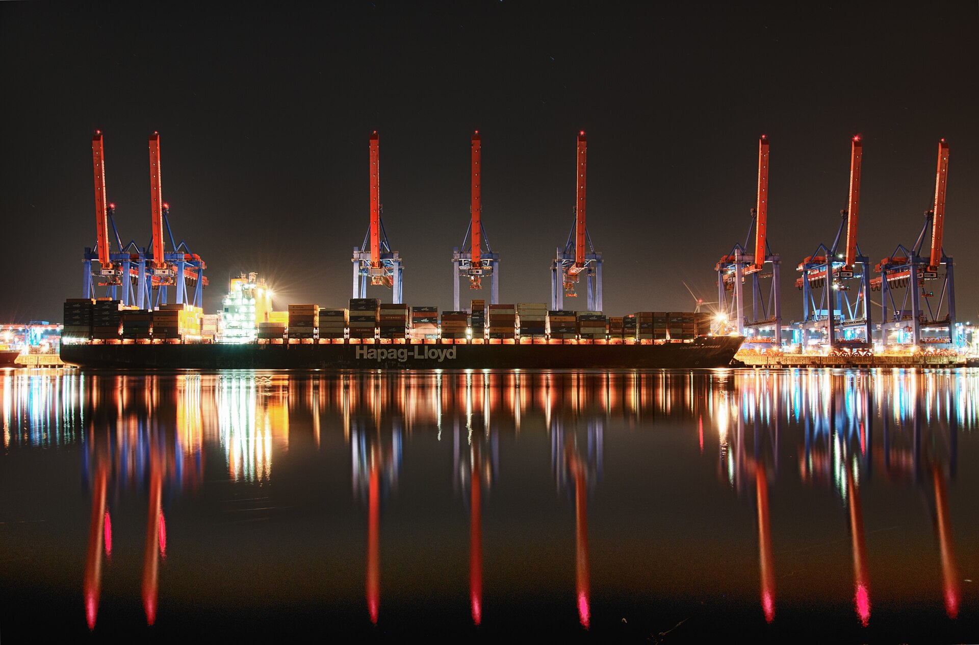 Container ship at a port terminal at night with cranes reflected in the water